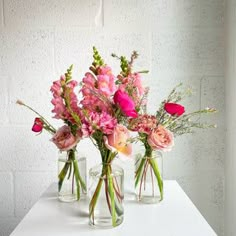 three clear vases with pink flowers on a white table