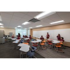 students are sitting at desks in an empty classroom with whiteboards on the wall