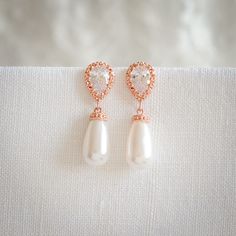 a pair of pearl and rose gold earrings on a white cloth with pearls in the shape of hearts