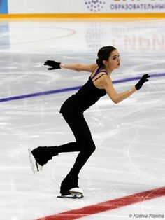 a woman skating on an ice rink wearing black clothes and holding her arms out in the air