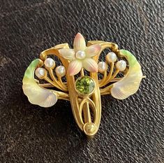 An enchanting Art Nouveau era flower pin by American maker Whiteside & Blank with iridescent enameling and a peridot center.  The soft pink petals remind us of cherry blossoms while the green enameled leaves look like samara seeds!  Wonderfully detailed with pearl accents.  The pin is stamped with the maker's mark along with faded marks for 14K stamps. Metal: 14K Yellow Gold Weight: 6.1 grams Measurement: 1 inch long by 1.1 inches wide Markings: Maker's mark Condition: In very good antique condition with some minor surface wear consistent with age.  One petal may have had the enamel touched up previously. Follow us on Instagram @alphaomegajewelry for the latest updates from our shop!  We have lots of fun there and add videos, highlights, and showcase our newest acquisitions. Pink Petals, Enamel Flower, Maker's Mark, Flower Pins, Samara, Cherry Blossoms, Makers Mark, Soft Pink, Antique Jewelry