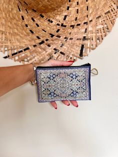 a woman's hand is holding a small purse in front of a straw hat