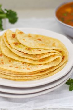 a white plate topped with tortillas next to a bowl of soup and cilantro