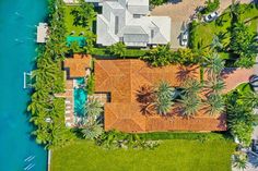 an aerial view of a house with palm trees in the foreground and blue water in the background