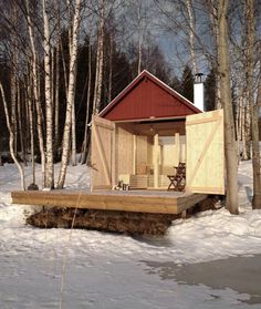 a small cabin in the middle of some snow covered ground with chairs and trees around it