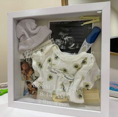 a baby's clothes and hairbrush are in a shadow box on a table