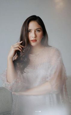 a woman in a white dress sitting on a couch with her hand near her face