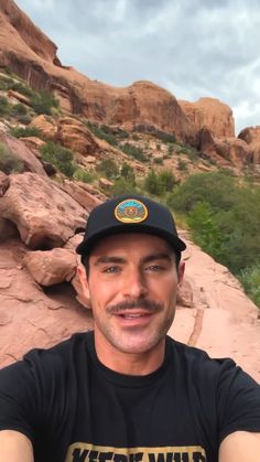 a man wearing a black hat is taking a selfie in front of some rocks