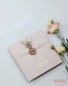 the wedding card is next to some flowers and a wax stamp on its front cover