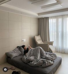 a man laying on top of a bed in a room with white walls and flooring