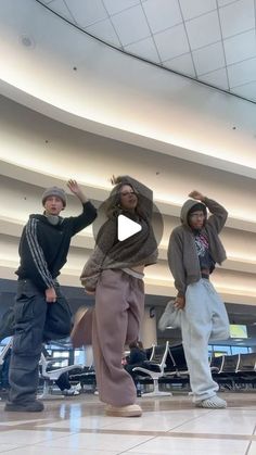 three people standing in an airport lobby with their arms up and one person wearing a hoodie