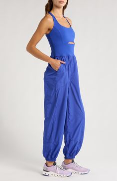 Go for a run in this one-and-done jumpsuit featuring a cutout knit tank with cross-back straps and eased-fit woven track pants. 56" length; 29" inseam; 11" leg opening (size Medium) Partially lined Scoop neck Front slant pockets; back zip pocket Elastic cuffs 68% nylon, 32% elastane with 100% polyester pants Machine wash, tumble dry By Free People; imported Summer Athleisure Activewear With Elastic Panels, Spring Athleisure Overalls Jumpsuit, Spring Stretch Jumpsuits And Rompers For Yoga, Spring Yoga Stretch Jumpsuits And Rompers, Spring Activewear With Elastic Side Panels, Sleeveless Jumpsuits And Rompers For Yoga In Spring, Spring Sleeveless Nylon Activewear, Relaxed Fit Jumpsuits And Rompers For Athleisure, Casual Jumpsuits And Rompers For Yoga In Spring