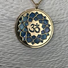 "Om in 24 carat gold on 925 silver and blue mother of pearl backdrop. Om is one of the most important spiritual symbols, a sacred sound in Indian religions, found also in some chapters of the Veda. It has variously been associated with concepts of \"cosmic sound\" that celebrates the creative powers of the Universe. Its sound is made up of three syllabes (A-U-M): wakefulness / darkness / present, dream / unconscious / past, deep sleep / future truth. In the jewel The five curves shaping the Om s Spiritual Round Mother Of Pearl Jewelry, Blue Hallmarked Amulet Necklaces, Spiritual Mother Of Pearl Jewelry With Gemstones, Spiritual Mother Of Pearl Pendant Necklace, Blue Spiritual Locket Jewelry, Spiritual Blue Medallion Necklaces, Blue Medallion Necklace For Spiritual Style, Blue Medallion Spiritual Necklaces, Spiritual Gold Necklace With Mother Of Pearl