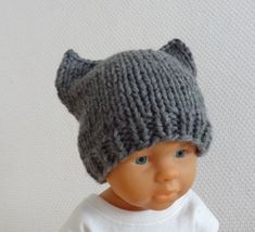 a baby doll wearing a knitted hat with horns on it's head, standing against a white background