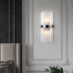 a modern wall light with three lights on it's side and a plant in the corner