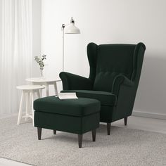 a green chair and footstool in a white living room with a small table