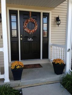 a black front door with two flower pots and a wreath on the side of it