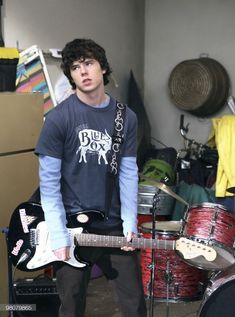 a young man holding an electric guitar while standing in front of a recording equipment set