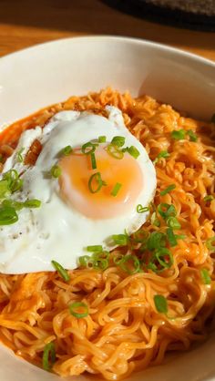 a white bowl filled with noodles and topped with an egg on top, sitting on a wooden table