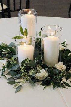 three white candles are sitting on a table with greenery