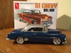 an old model car sitting on top of a wooden table next to a sign that says 51 chevy bel air