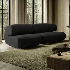 a living room with a large black couch and coffee table in front of two windows