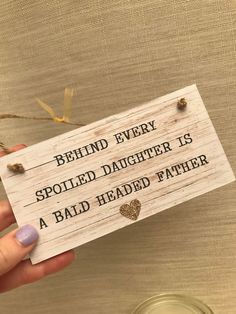 a hand holding a sign that says behind every spoiled daughter is a bald head father