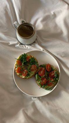 two open faced sandwiches on a white plate next to a cup of coffee and saucer