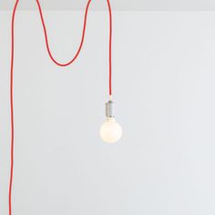 a red cord is connected to a light bulb on a white wall with a gray background