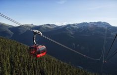 a red cable car going up the side of a mountain with mountains in the background