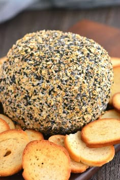 sesame seed cheese ball on a plate with crackers and garlic flakes around it