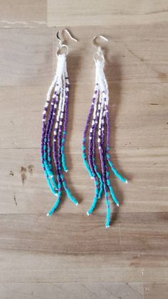 two purple and blue beads are hanging from silver hooks on a wooden surface with wood flooring