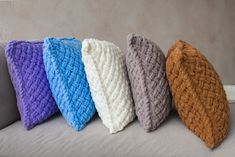 four knitted pillows lined up on a couch in different colors and sizes, all sitting side by side