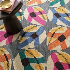 an area rug with multicolored flowers on it and a gold vase next to it