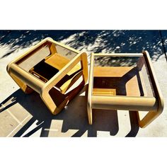 two wooden chairs sitting next to each other on top of a cement floor near a tree