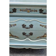 an antique dresser with blue paint and gold decorations on the top, sitting in a carpeted area