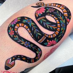 a black and white snake tattoo on the right thigh, with colorful flowers around it