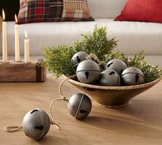 a bowl filled with metal bells sitting on top of a wooden table next to candles