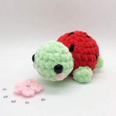 a crocheted red and green turtle next to a tiny pink flower