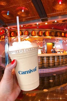 a hand holding up a drink in front of a bar with neon signs on the walls