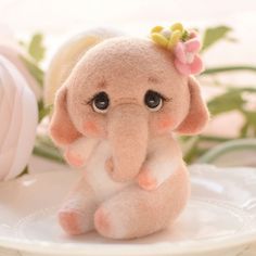 a small stuffed elephant sitting on top of a white plate next to a pink flower