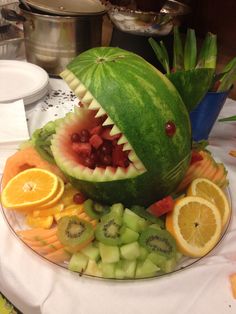 a watermelon shaped like a shark with its mouth open and fruits in the foreground