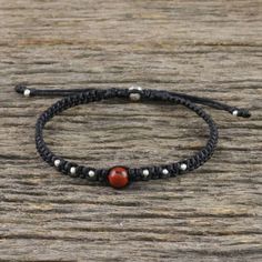 a red beaded bracelet sitting on top of a wooden table next to a black string