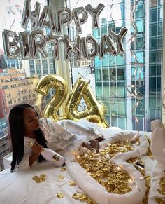 a woman laying on top of a bed covered in gold confetti and balloons