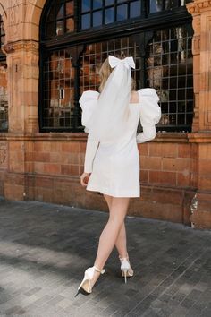 a woman in a short white dress is walking down the street with her back to the camera