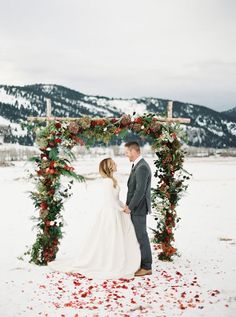 a bride and groom standing under an arch decorated with flowers in the snow at their winter wedding