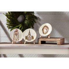 three small plates with designs on them sitting on a shelf in front of a wreath