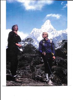 two men standing next to each other on top of a mountain