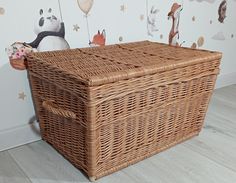 an empty wicker basket sitting on the floor in front of a wall with animals and balloons