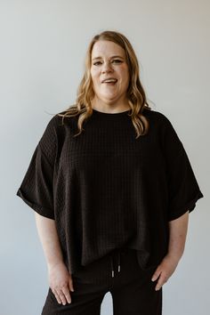 A person with long hair stands against a plain white background, wearing Mikarose's textured oversized tee with rolled cuffs and a scooped neckline, along with matching pants. Textured Crew Neck Top For Layering, Knit Textured Tops For Layering, Textured Crew Neck Tops For Fall, Textured Knit Short Sleeve Top For Loungewear, Textured Casual Crew Neck Tops, Textured Crew Neck Casual Tops, Textured Relaxed Fit Crew Neck Top, Relaxed Fit Textured Crew Neck Top, Casual Textured Crew Neck Top